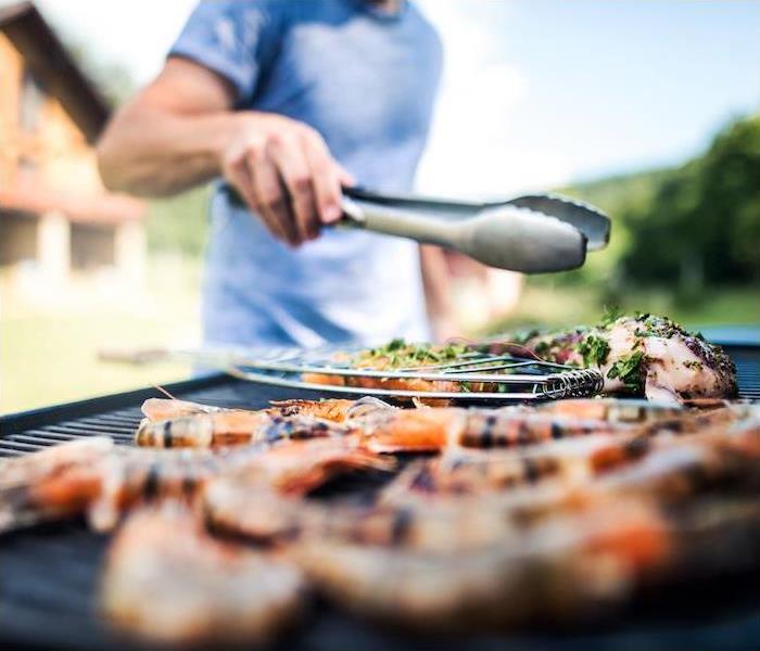 Man holding tongs above grill preparing food outdoors